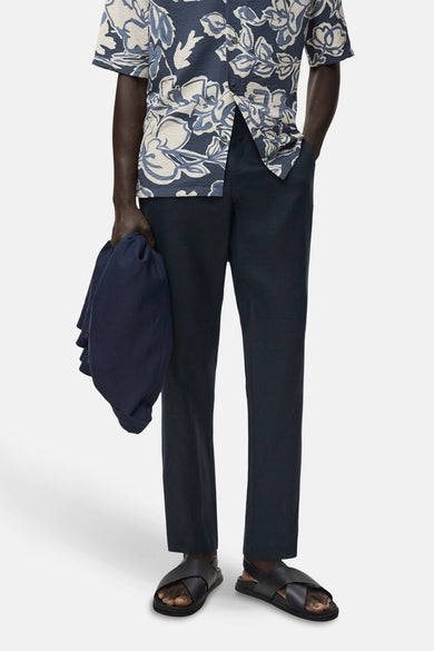 Blauwe broek van MANGO, met een effen textuur, gecombineerd met een bloemenprint overhemd en zwarte sandalen.

