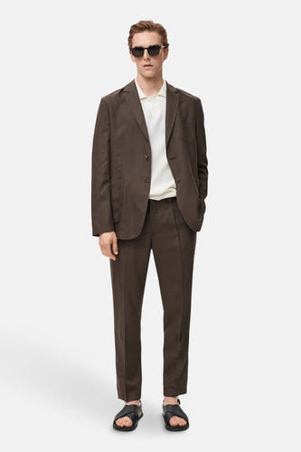 Bruine blazer van MANGO, gedragen met een wit poloshirt, een bijpassende pantalon en zwarte sandalen.

