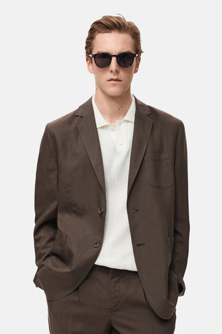 Blazer marron de MANGO porté sur un polos blanc avec des lunettes de soleil, pour une apparence décontractée et élégante.