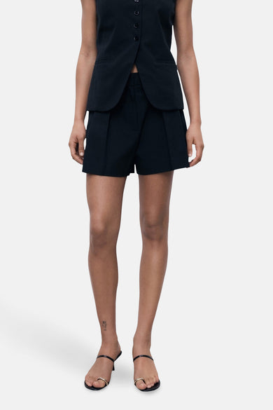 Zwarte bermuda van MANGO, met plooien aan de voorkant, gecombineerd met een zwart vest en zwarte sandaaltjes.
