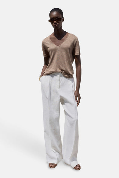 T-shirt marron à manches courtes de MANGO, avec col V et associé à un short en lin blanc.