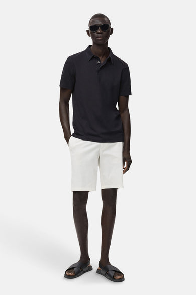 Polo bleu marine à manches courtes de MANGO, porté avec un short blanc et des sandales noires.