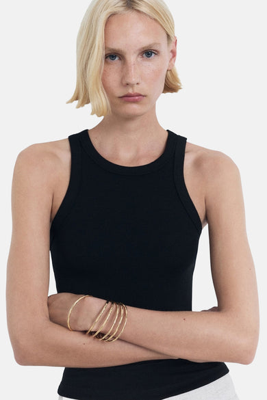 Zwarte singlet van MANGO, met gekruiste armen met gouden armbanden, tegen een witte achtergrond.