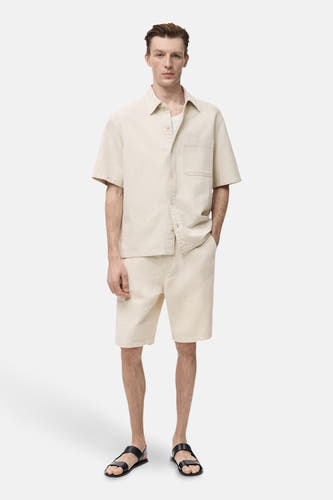 Jeanshemd in ecru van MANGO, met korte mouwen en een borstzak, gedragen met bijpassende shorts en sandalen.
