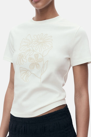 Ecru T-shirt met korte mouwen van MANGO, met bloemenborduurwerk op de voorkant en gedragen met een zwarte rok.
