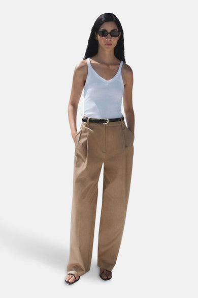 Beige broek van MANGO, met plooien, wijde pijpen, een zwarte riem en zwarte sandalen.
