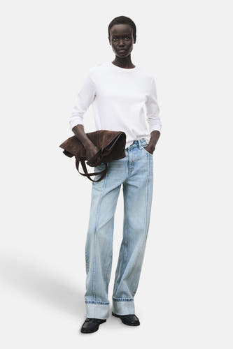 Jean droit bleu clair de MANGO, avec des poches froncées et porté avec un t-shirt blanc et une poche marron.