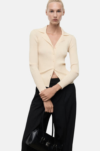 Cardigan jaune de MANGO, avec des manches longues, un col et une fermeture à boutons devant, porté avec un pantalon noir et une pochette.