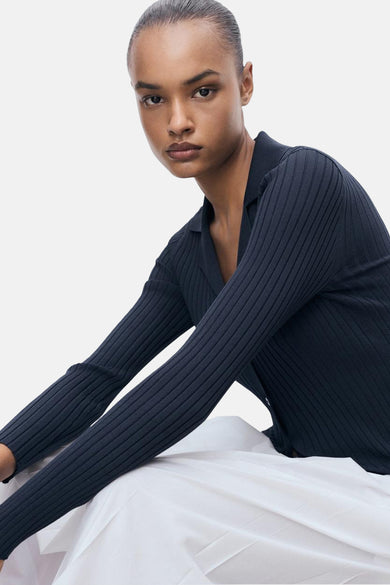 Cardigan bleu de MANGO, avec des manches longues et un col, porté sur un pantalon blanc.