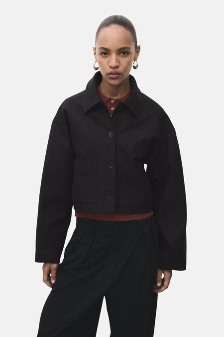 Zwarte blazer van MANGO, met lange mouwen en knoopsluiting, gecombineerd met een bruine top en zwarte pantalon.
