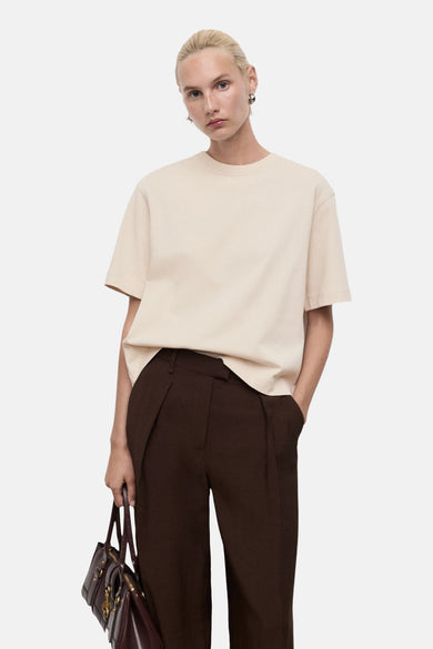 Beige T-shirt met korte mouwen van MANGO, gedragen met bruine pantalon en een bordeauxrode handtas.