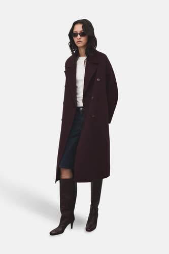 Bordeaux long manteau de MANGO, porté avec un chemisier blanc, une jupe en denim et des bottes hautes.