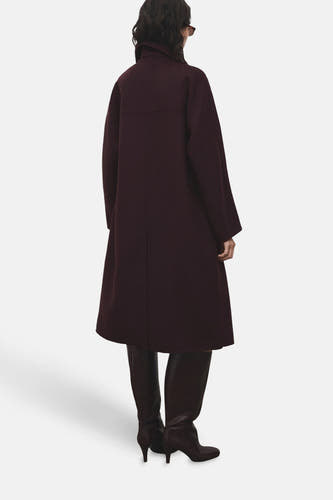 Manteau long MANGO de Bordeaux, vu de l'arrière avec une col montée et porté avec des bottes en cuir marron.