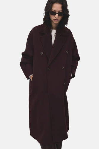 Manteau long de MANGO, avec des boutons doubles et des poches, porté avec un haut blanc et des lunettes de soleil.