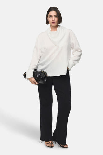 Witte blouse met lange mouwen van MANGO, met een speciale kraag en gedragen met een zwarte broek en handtas.
