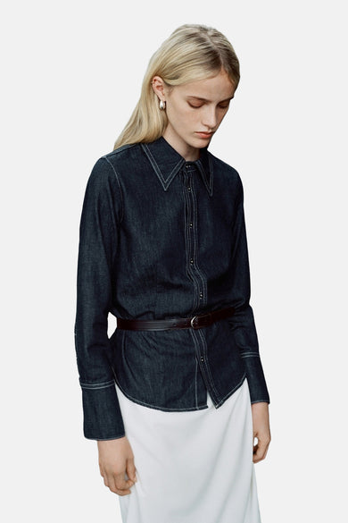 Donkerblauw denim overhemd met lange mouwen van MANGO, afgewerkt met witte stiksels en een smalle riem.

