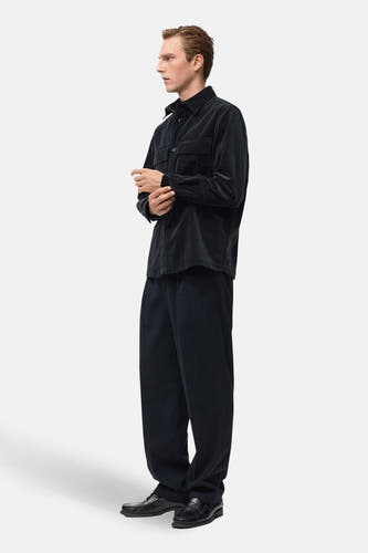 Veste courte bleue de MANGO, à manches longues et deux poches poitrine, portée avec un pantalon large et des chaussures en cuir.