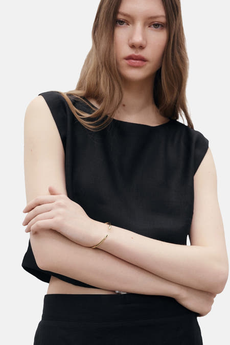 Blouse sans manches noire de MANGO, avec des bras croisés et un bracelet doré.
