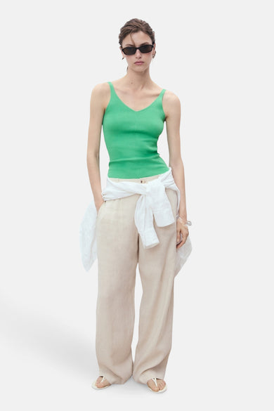 Groene singlet van MANGO, gedragen met een wit overhemd om de taille geknoopt en een beige broek.
