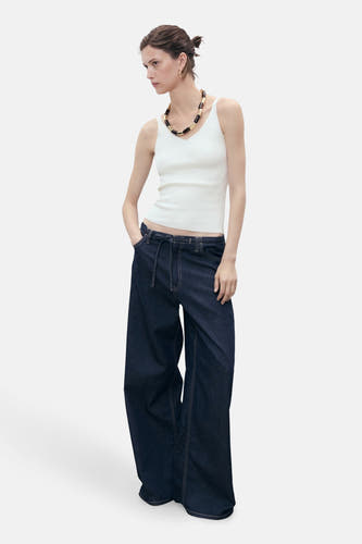 Witte singlet van MANGO, met een V-hals en gedragen met een opvallende halsketting en wijde jeans.

