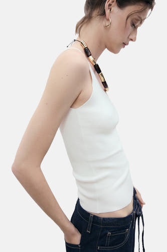 Witte singlet van MANGO, getailleerd model gedragen met een donkerblauwe jeans en een opvallende halsketting, zijaanzicht.

