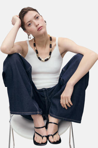 Witte singlet van MANGO, gedragen met wijde jeans en zwarte sandalen in een lifestyle setting.