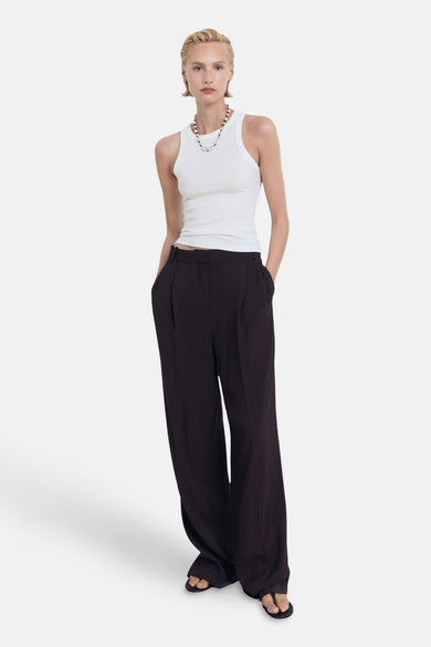 Witte singlet van MANGO, gedragen met wijde, donkerbruine pantalon en een kralenketting.