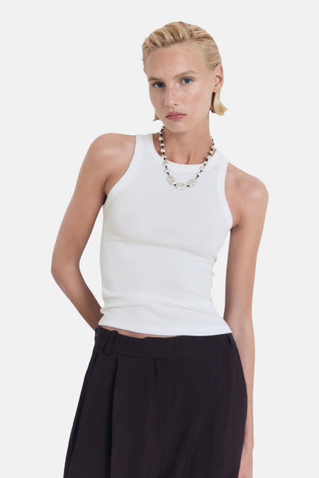 Witte singlet van MANGO, gedragen met een ketting met kralen en een donkere broek.