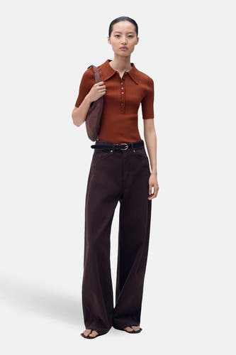 Pull marron avec col rond de MANGO, à manches courtes et fermeture à boutons, associé à un pantalon marron et une sacoche.