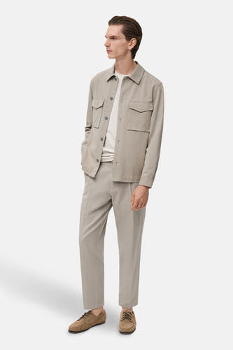 Beige hemd met lange mouwen van MANGO, met zakken en gedragen met een wit T-shirt en beige broek.
