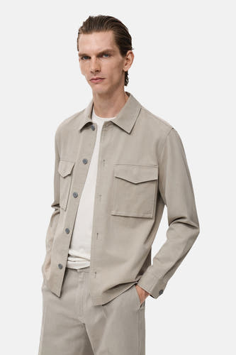 Beige overhemd met lange mouwen van MANGO, met zakken en knopen, gedragen over een wit T-shirt en een beige broek.
