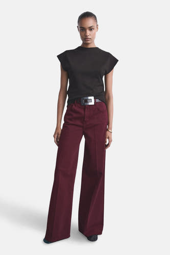 Bordeauxkleurige jeans van MANGO, wijd uitlopend met een riem met zilverkleurige gesp, gecombineerd met een zwart shirt.