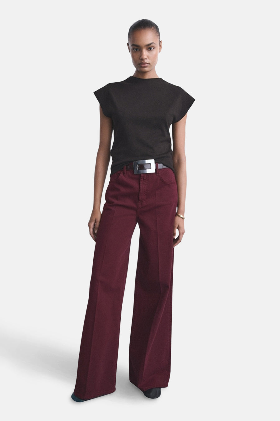 Bordeauxkleurige jeans van MANGO, wijd uitlopend met een riem met zilverkleurige gesp, gecombineerd met een zwart shirt.