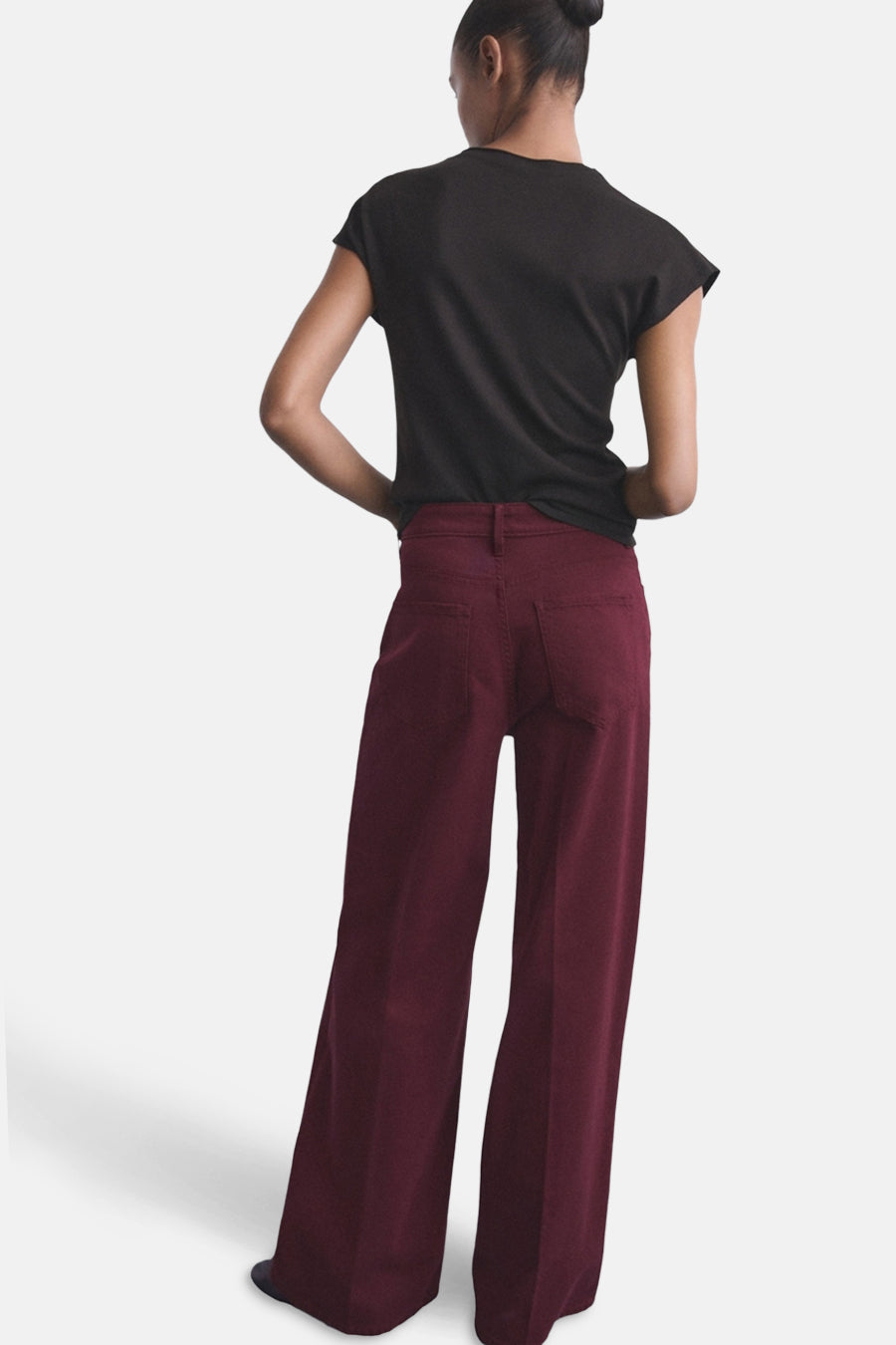 Bordeaux gekleurde jeans van MANGO, gezien van achteren met een zwarte top en opgestoken haar.