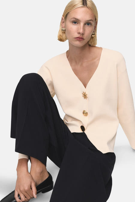 Ecru gilet van MANGO met decoratieve knopen, gecombineerd met zwarte broek en zwarte schoenen.
