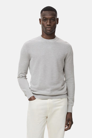 Sweat-shirt gris à col rond de MANGO, porté avec un pantalon blanc et une main dans la poche.