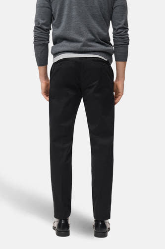 Pantalon bleu marine de MANGO, vu du dos, combiné avec un pull gris et des chaussures noires.