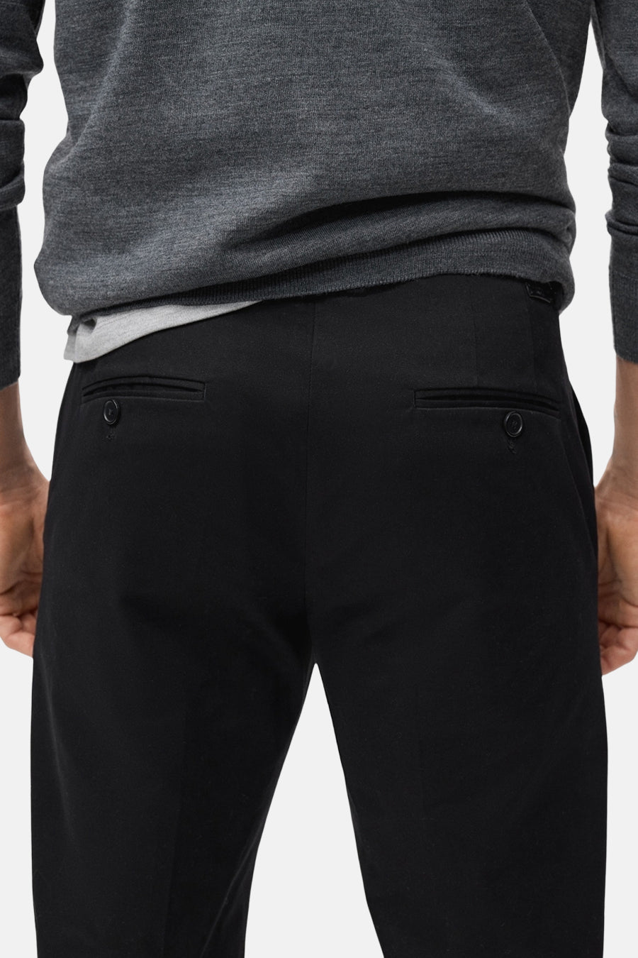 Pantalon noir de MANGO, avec des poches arrière à boutons, associé à un pull gris.