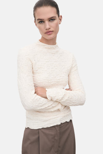 T-shirt beige à longues manches de MANGO, avec une texture unique froissée et associé à des pantalons bruns.