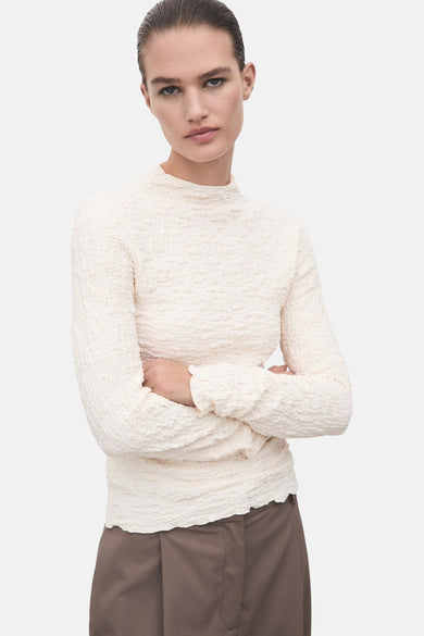 T-shirt beige à longues manches de MANGO, avec une texture unique froissée et associé à des pantalons bruns.