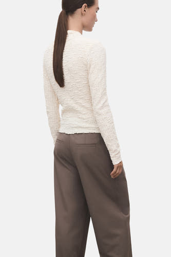 Beige T-shirt met lange mouwen van MANGO, met een unieke gerimpelde textuur en gecombineerd met bruine broeken.
