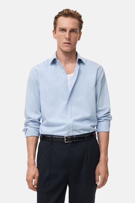 Blauw overhemd met lange mouwen van MANGO, gedragen met een witte tanktop en donkere pantalon met riem.
