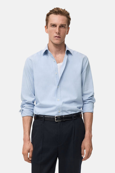 Blauw overhemd met lange mouwen van MANGO, gedragen met een witte tanktop en donkere pantalon met riem.
