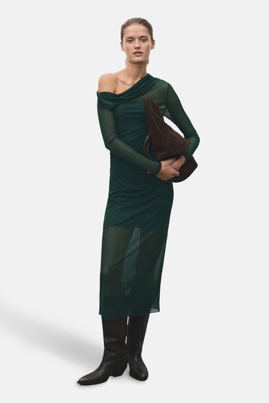 Robe verte à longues manches de MANGO, avec une ligne d'épaule unique et un tissu transparent, portée avec des bottes brunes.