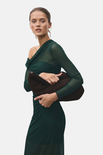 Vrouw in groene jurk houdt bruine handtas vast.