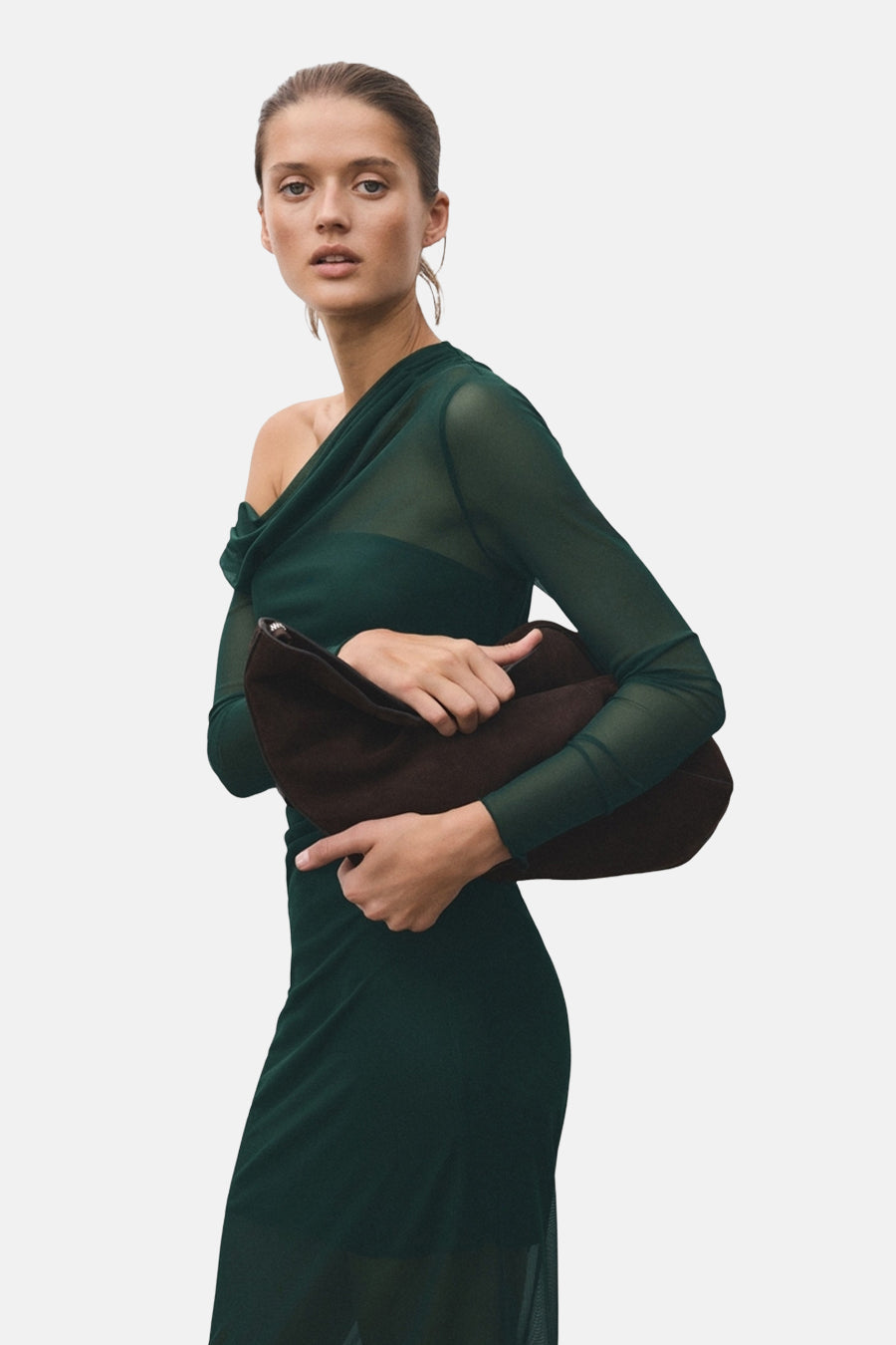 Vrouw in groene jurk houdt bruine handtas vast.