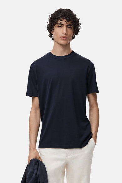 T-shirt bleu à manches courtes de MANGO, porté avec un pantalon beige et une veste dans la main.