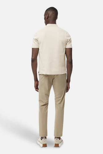 Beige broek van MANGO, gezien van achteren, gecombineerd met een crèmekleurig poloshirt en lage sneakers.