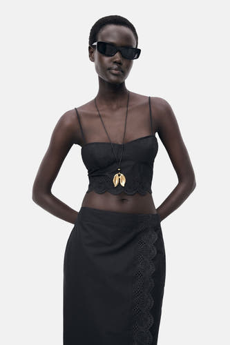 Zwarte spaghettitop van MANGO, met broderie anglaise details langs de onderrand, gedragen met een gouden ketting.
