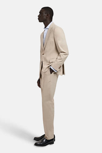 Beige kostuumbroek van MANGO, in een effen kleur, gezien in zijaanzicht met een bijpassend jasje en zwarte schoenen.
